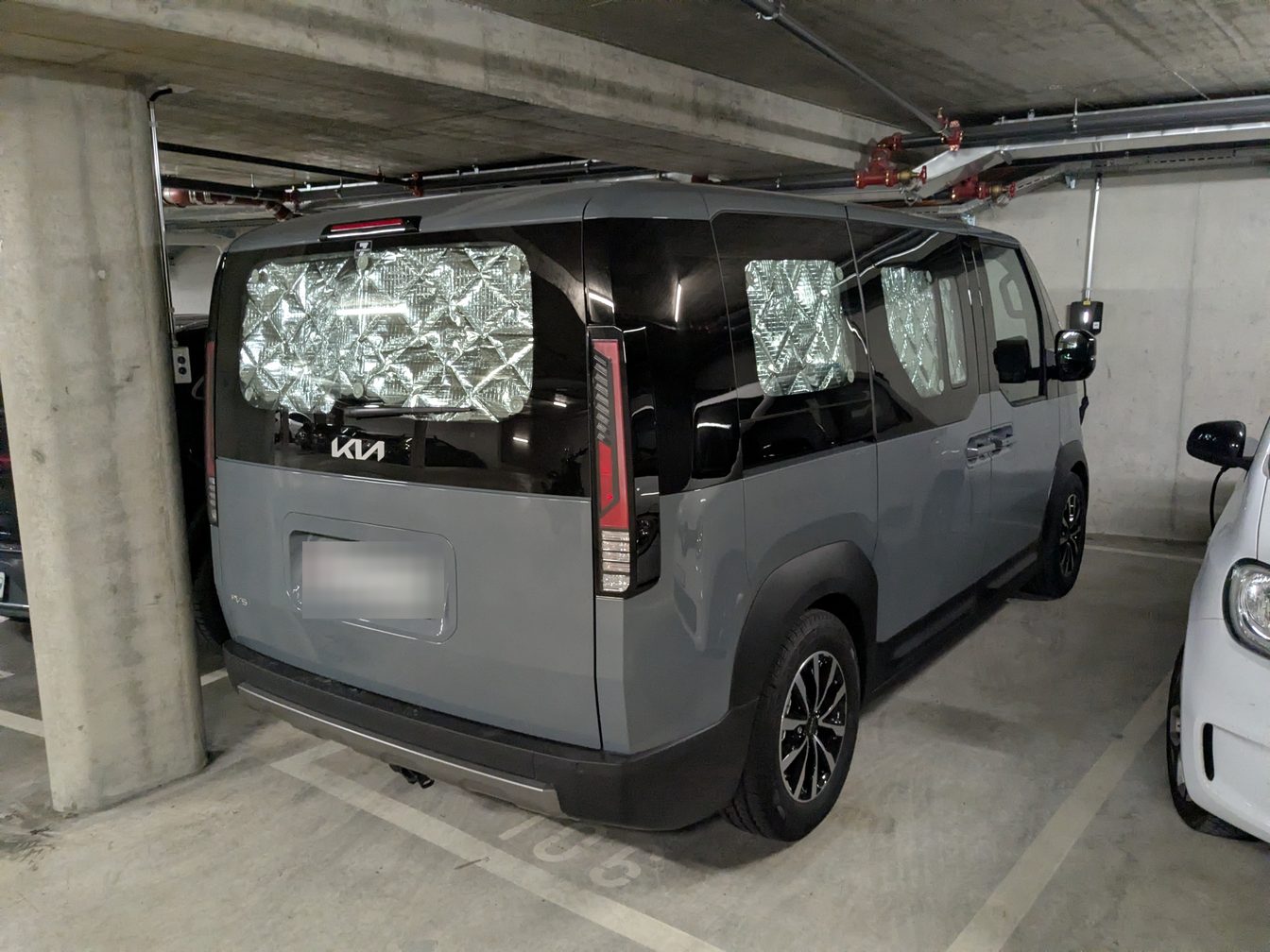 L'arrière du van gris dans un parking souterrain : la lunette arrière et deux vitres latérales couvertes de rideaux isolants argentés.